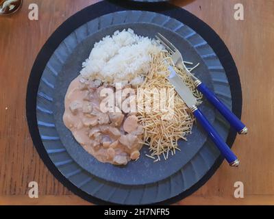 Brazilian Beef Stroganoff with Straw Potatoes, isolated on a placemat on a wooden table. Top view. Stock Photo