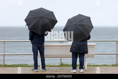 24 November 2021, Mecklenburg-Western Pomerania, Kühlungsborn: With umbrellas two walkers stand on the waterfront and look at the Baltic Sea. Many clouds and drizzle provide classic North German dirty weather. Photo: Bernd Wüstneck/dpa-Zentralbild/ZB Stock Photo