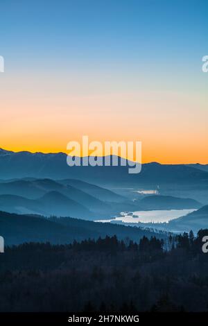 colourful evening dawns over the mountains, dam and wooded landscape below Stock Photo