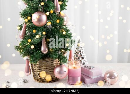 Modern pastel pink color baubles decorations hanging on Christmas tree in home living room, with pink gifts and candle burning. Pastel pink style Chri Stock Photo