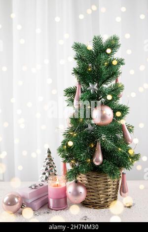Modern pastel pink color baubles decorations hanging on Christmas tree in home living room, with pink gifts and candle burning. Pastel pink style Chri Stock Photo