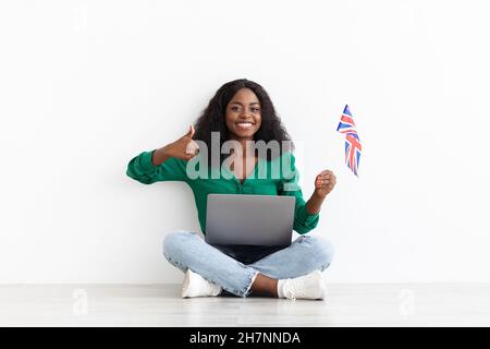 Black lady with laptop and UK flag showing thumb up Stock Photo