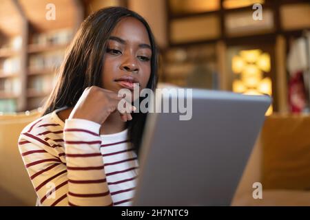 Thoughtful young black woman looking at tablet screen, working or studying online from home Stock Photo
