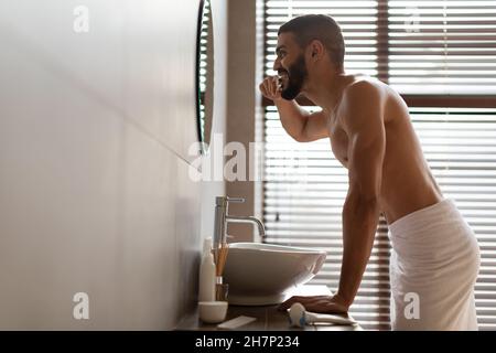 Handsome young Arab man using toothbrush in bathroom, profile view Stock Photo