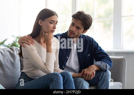 Careful european millennial man calms unhappy sad offended woman after quarrel in living room interior Stock Photo