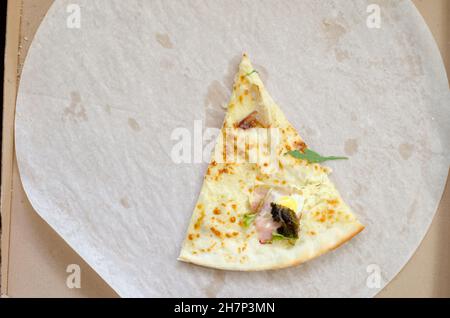One slice of pizza in a large cardboard box. The last slice of pizza with herbs and bacon. Stock Photo