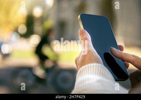 Woman's hand holding a mobile and making a message in the street Stock Photo