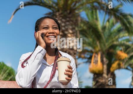 Smiling african american woman talking with mobile with a take away coffee in hand Stock Photo