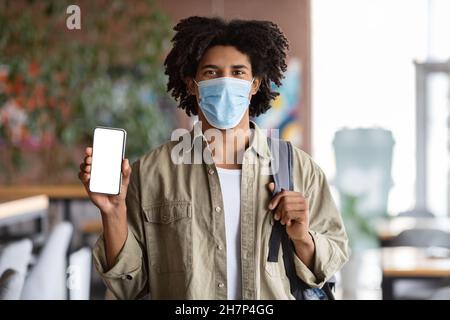 Safety Measures. Black Guy Wearing Medical Mask Showing Blank Smartphone At Cafe Stock Photo