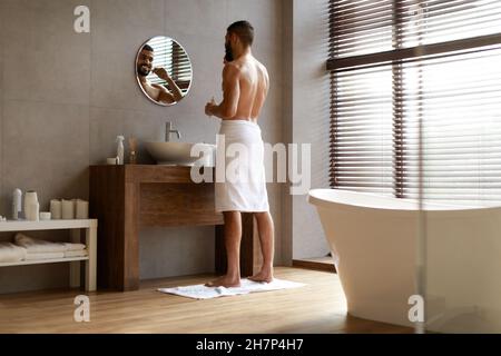 Handsome young Arab man using toothbrush in bathroom Stock Photo