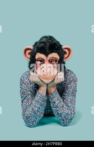 closeup of a young man, wearing a monkey mask, looking to the observer while is lying down on a blue background Stock Photo