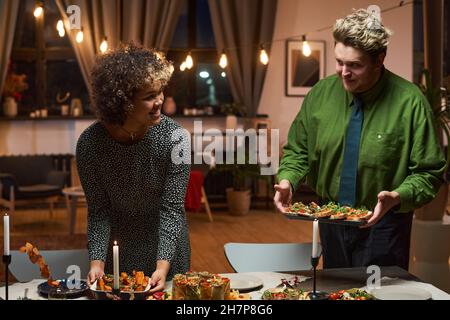 Young couple setting appetizers on dining table, they arranging dinner party for friends Stock Photo
