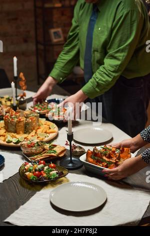 Close-up of couple carrying different appetizers on dining table, they preparing for dinner party Stock Photo