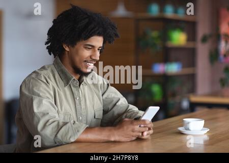 Young African American Guy Using Smartphone While Sitting At Tablet In Cafe Stock Photo