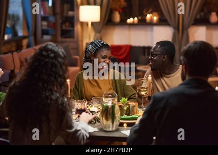 African young couple sitting at dining table and laughing while meeting with friends at dinner party Stock Photo