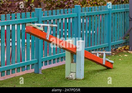 Red Seesaw at Children Playground With Wooden Fence Stock Photo