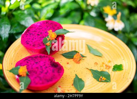 Vibrant colors of Dragon Fruit cut in half displayed on a yellow plate with flowers and leaves for décor. Stock Photo