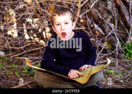 Child with astonished expression to find the location on an old map of a treasure in a forest. Stock Photo