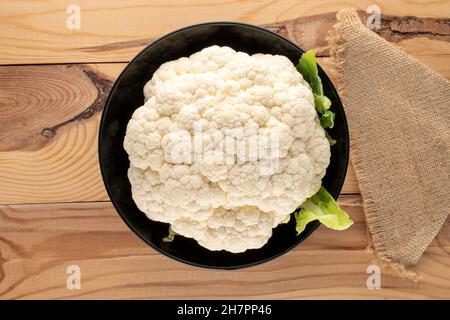 One ripe cauliflower in a black plate on a wooden table, close-up, top view. Stock Photo