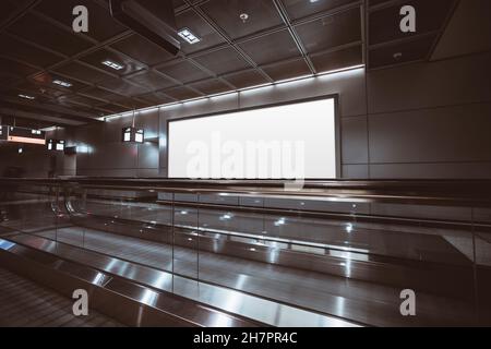 A big rectangular glowing blank neon billboard template near two travelators of a modern dark airport terminal; a mockup of an empty white banner indo Stock Photo