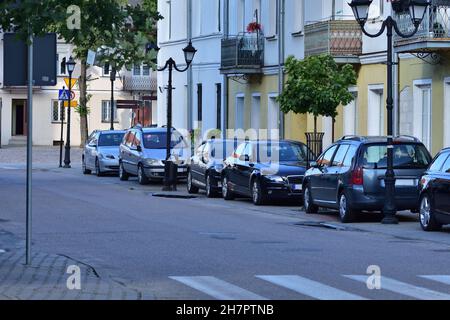 Passenger cars standing in a car park separated from the public road next to residential houses. Stock Photo