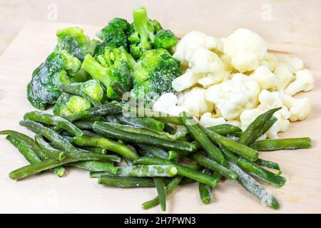 Different frozen vegetables (broccoli, green beans, cauliflower) on light wooden background. Stock Photo