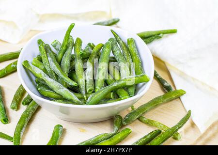 Frozen green beans pods in white bowl on light wooden background. Stock Photo