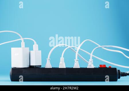 Surge protector with connected white wires of electrical appliances on a blue background. Free space Stock Photo