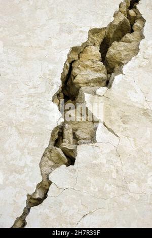 Big diagonal crack in wild shell stone masonry covered with plaster. Consequences of earthquake. Copy space. Close-up. Selective focus. Stock Photo