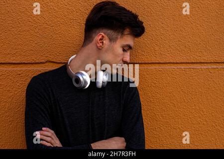 Handsome Spanish male with a headphone leaning on a wall Stock Photo