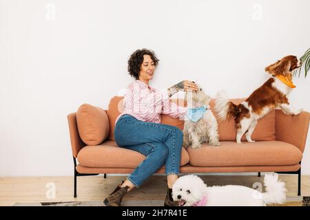 Young woman sitting on a couch with three dogs in living room Stock Photo