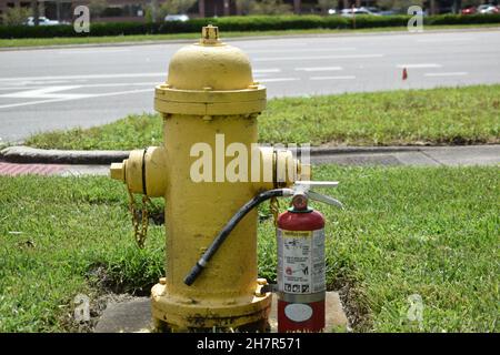 A portable fire extinguisher next to a yellow fire hydrant. Stock Photo