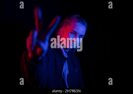 Colorful portrait of a confident blonde woman showing peace or victory sign on black backgound Stock Photo