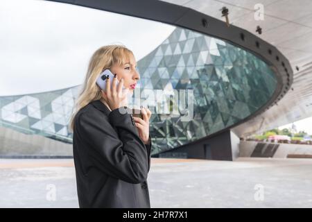 Entrepreneurial Caucasian woman having phone call against modern glass building Stock Photo