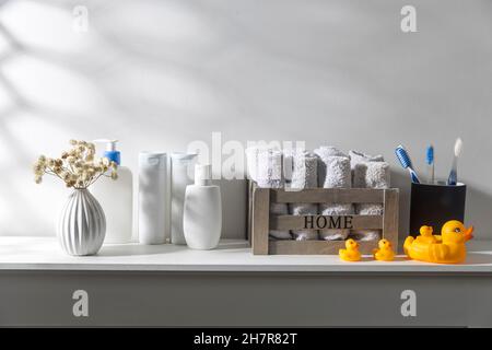 Shelf in the bathroom. Bouquet of gypsophila in white corrugated vase in style of the seventies, bottles of shampoo and cream, small face towels in co Stock Photo