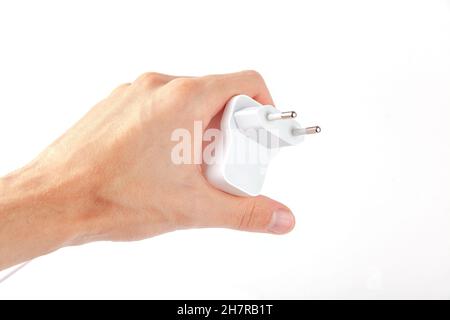 Man holding a simple white wired phone charger, EU plug, generic smartphone charger held in hand isolated on white, cut out. Consumer electronics indu Stock Photo