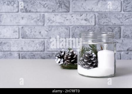 White candle in a glass vase with pine cones and spruce branches on a black and gray background. The concept of candlesticks in the interior of the ki Stock Photo