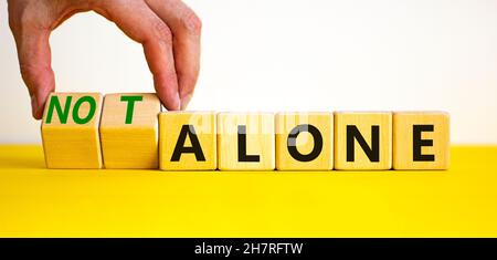 You are not alone symbol. Businessman turns wooden cubes and changes words alone to not alone. Beautiful yellow table white background, copy space. Bu Stock Photo