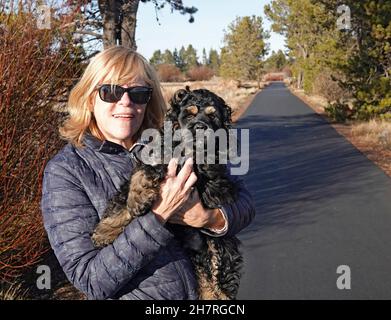 A middle-aged woman on a country walk with her Amcerican Cocker Spaniel puppy, in Sunriver, Oregon. Stock Photo