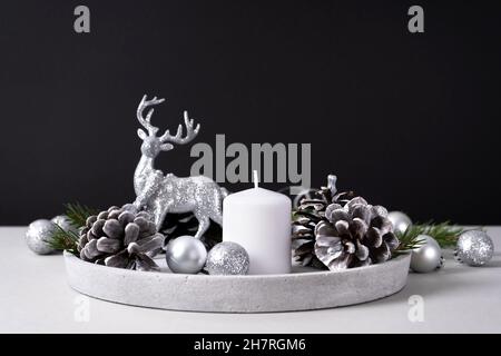 White candle on a concrete tray with pine cones, fir branches and silver Christmas balls with a deer on gray and black background. Interior for Christ Stock Photo