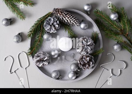 A concrete tray with a candle, pine cones, spruce branches, silver Christmas balls and numbers of the upcoming new year on a gray background. 2023. To Stock Photo