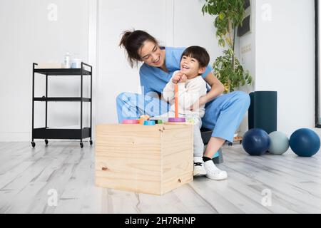 Therapist doing development activities with a little boy with cerebral palsy, having rehabilitation, learning . Training in medical care center. High quality photo. Stock Photo