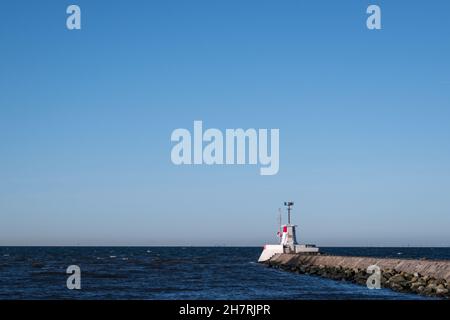 A white and red lighthouse situated on a stone pier and wave break at the port entry in Lomma Sweden