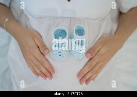 Crop unrecognizable woman lying with baby shoes on tummy Stock Photo