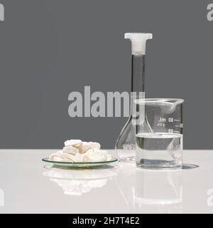 Closeup chemical ingredient on white laboratory table. Calcium carbonate Chip in Chemical Watch Glass place next to beaker with alcohol and Volumetric Stock Photo