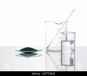 Zinc Powder in chemical watch glass place next to crystal clear liquid in beaker. Closeup chemical ingredient on white laboratory table. Side View Stock Photo