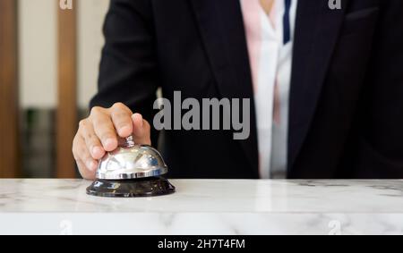 Closeup of a businesswoman hand ringing silver service bell on hotel reception desk. Stock Photo