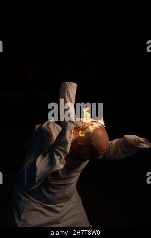 Bald man in a straitjacket with a burning head on a dark background. Stock Photo