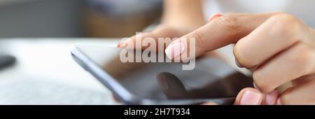 Girl presses finger on screen of smartphone on table is laptop Stock Photo