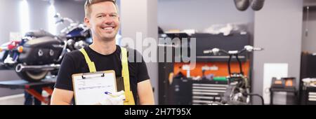 Young male locksmith in uniform stands in workshop and holds clipboard with documents in hands Stock Photo